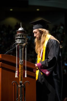 photo of dillon in graduation garb speaking at a podium
